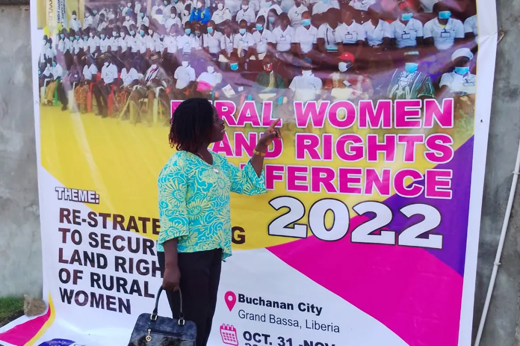 A women stands in front of a banner with the text Rural Land Rights Conference 2022