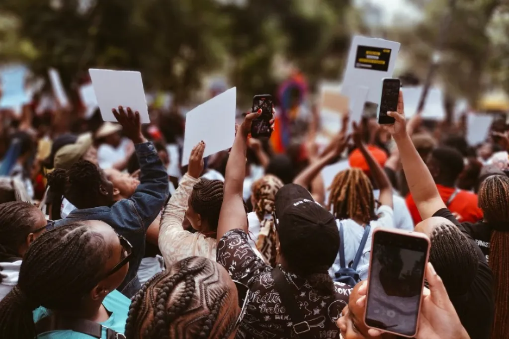 Människor demonstrerar i Kenya. Håller upp skyltar och mobiltelefoner.