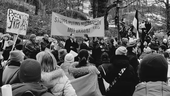 En svart och vit bild med människor som står på en demonstration till stöd för Ukraina. En banderoll med texten stoppa Putins krig i Ukraina.