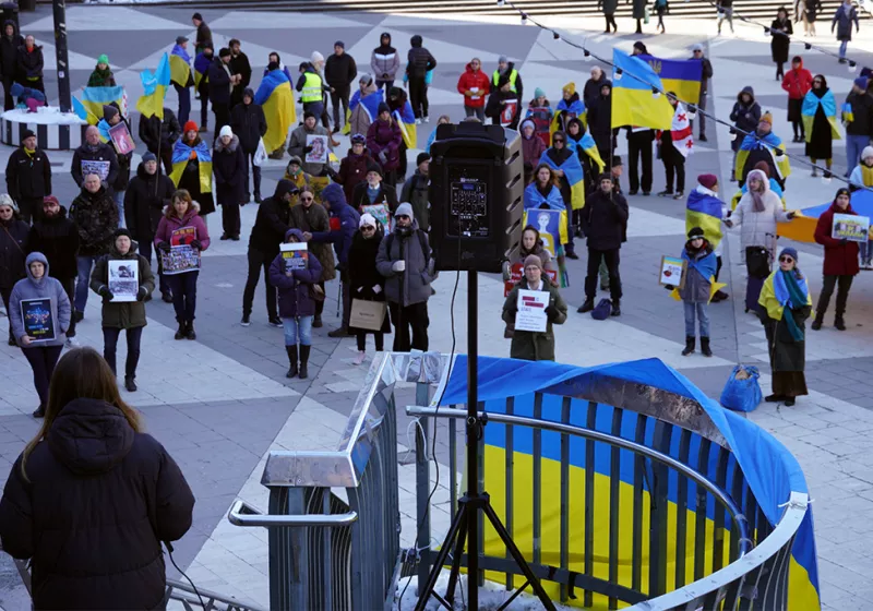 Svitlana talar framför en grupp demonstranter med plakat och ukrainska flaggor.