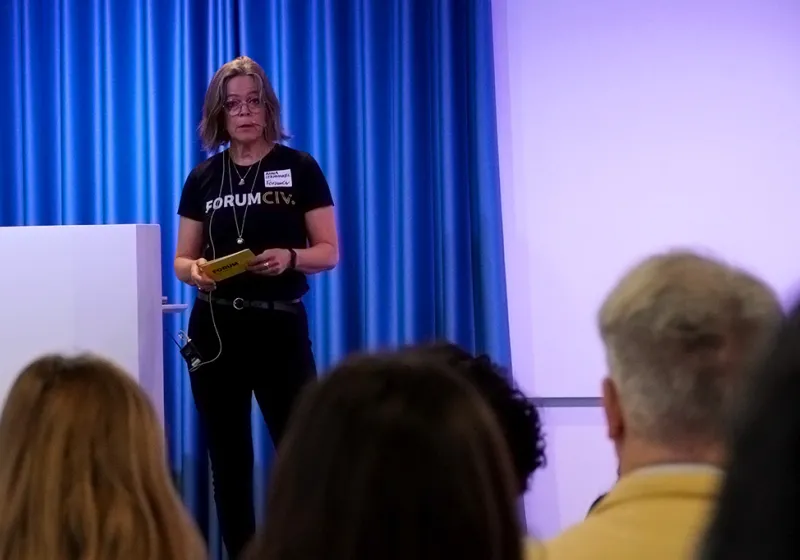 Anna talar till publiken på en scen. Hon har en svart t-shirt med texten ForumCiv.