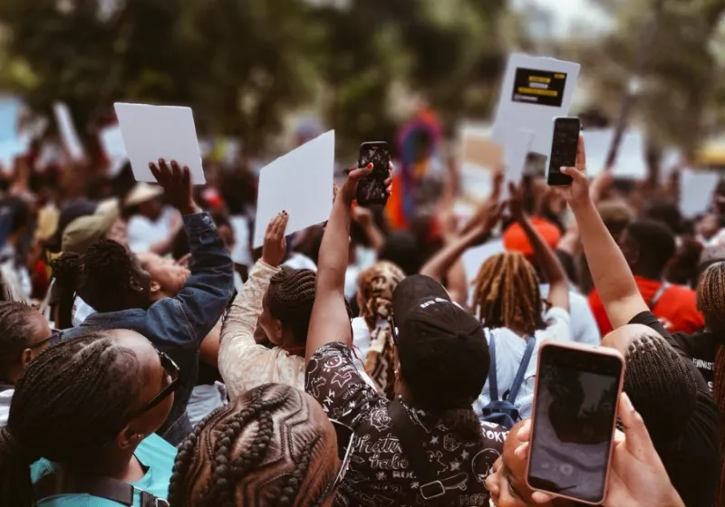 Människor demonstrerar i Kenya. Håller upp skyltar och mobiltelefoner.