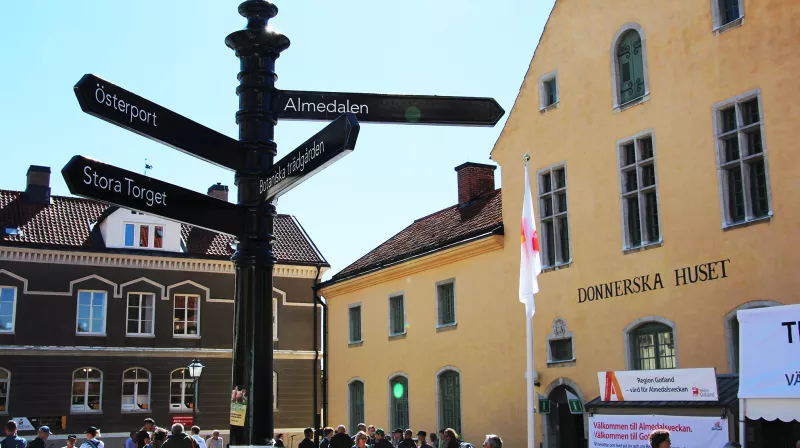A photo of a yellow building with the text Donnerska huset. On the left side there is a street sign that says Almedalen.