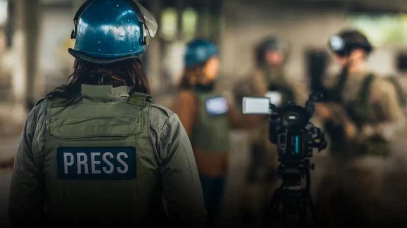Journalist wearing a protective vest with the text press and a blue helmet.